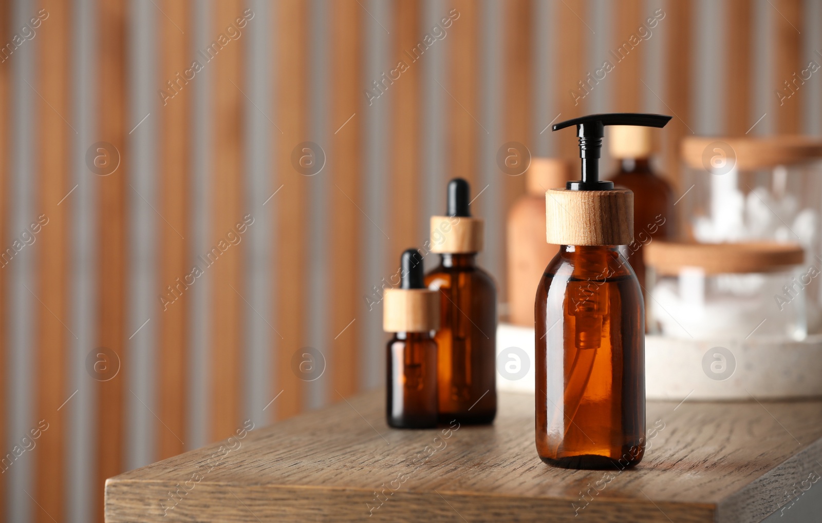 Photo of Bottle with dispenser cap and cosmetic products on wooden table indoors. Space for text