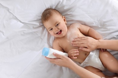 Photo of Mother applying dusting powder onto her baby on bed, top view