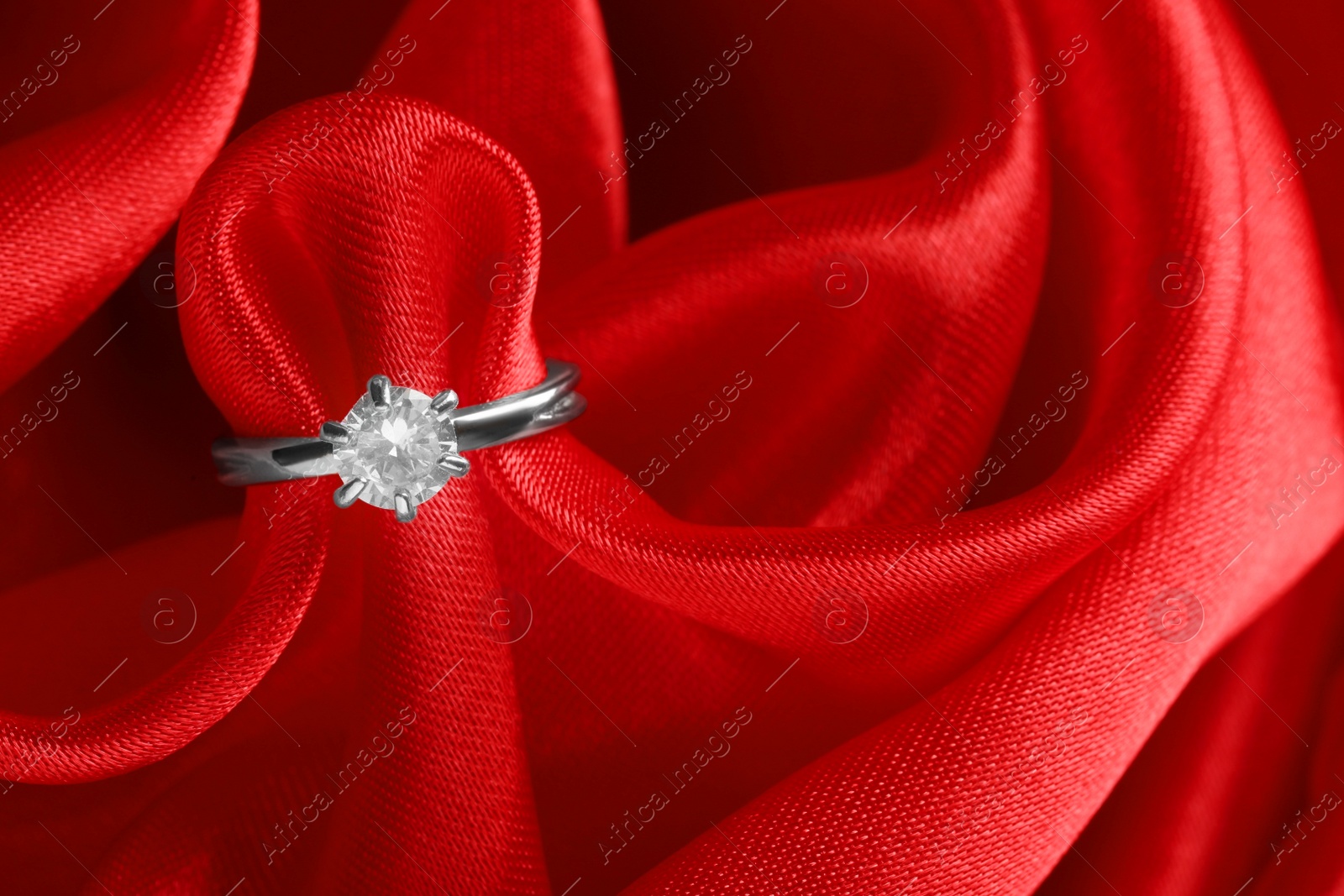 Photo of Beautiful luxury engagement ring with gemstone on red fabric, closeup