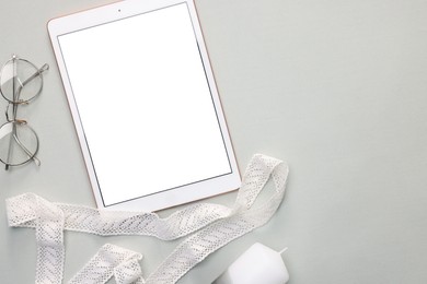 Modern tablet, glasses and ribbon on light grey background, flat lay. Space for text