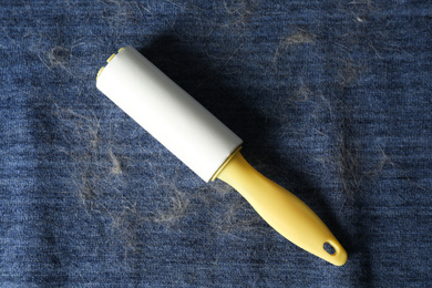 Photo of Lint roller on blue fabric covered with hair, top view