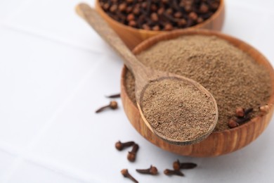 Photo of Aromatic clove powder in bowl, dried buds and spoon on white table, closeup. Space for text