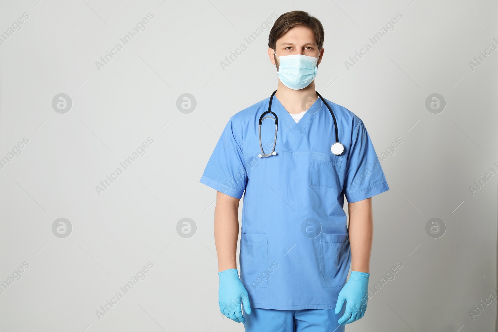 Photo of Doctor or medical assistant (male nurse) with protective mask and stethoscope on light grey background. Space for text