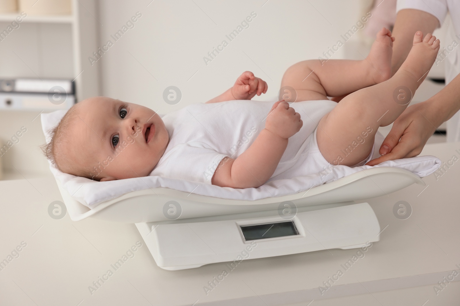 Photo of Pediatrician weighting cute little baby in clinic, closeup