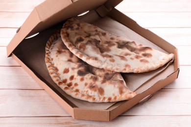 Photo of Cardboard box with delicious calzones on light wooden table