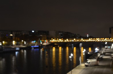 Blurred view of cityscape with bridge over river and buildings at night