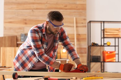 Photo of Carpenter shaping wooden bar with hand plane at table in workshop