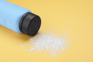 Photo of Bottle and scattered dusting powder on yellow background, space for text. Baby cosmetic product