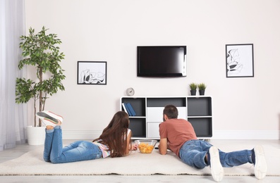 Photo of Young couple lying on carpet and watching TV at home
