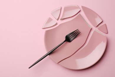 Photo of Pieces of broken ceramic plate and fork on pink background, flat lay. Space for text