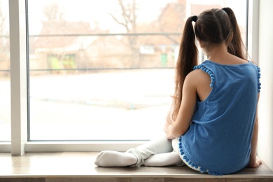 Photo of Lonely little girl sitting on windowsill. Autism concept