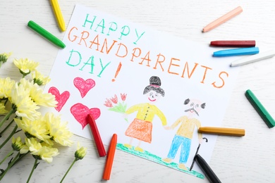 Photo of Beautiful drawing with phrase Happy Grandparents Day on white table, flat lay