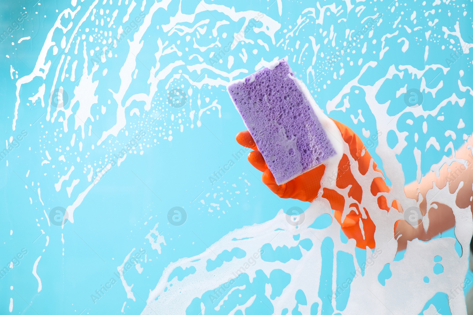 Photo of Woman cleaning glass with sponge against color background