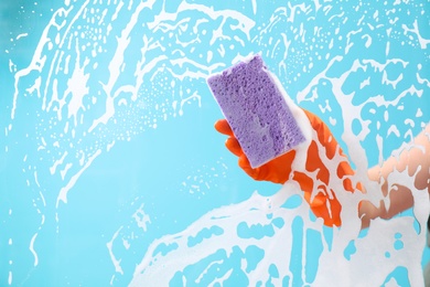 Photo of Woman cleaning glass with sponge against color background