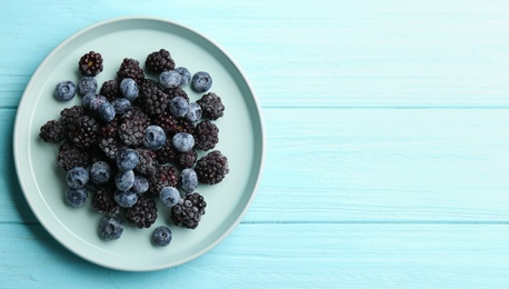 Photo of Tasty frozen blackberries and blueberries on light blue wooden table, top view. Space for text