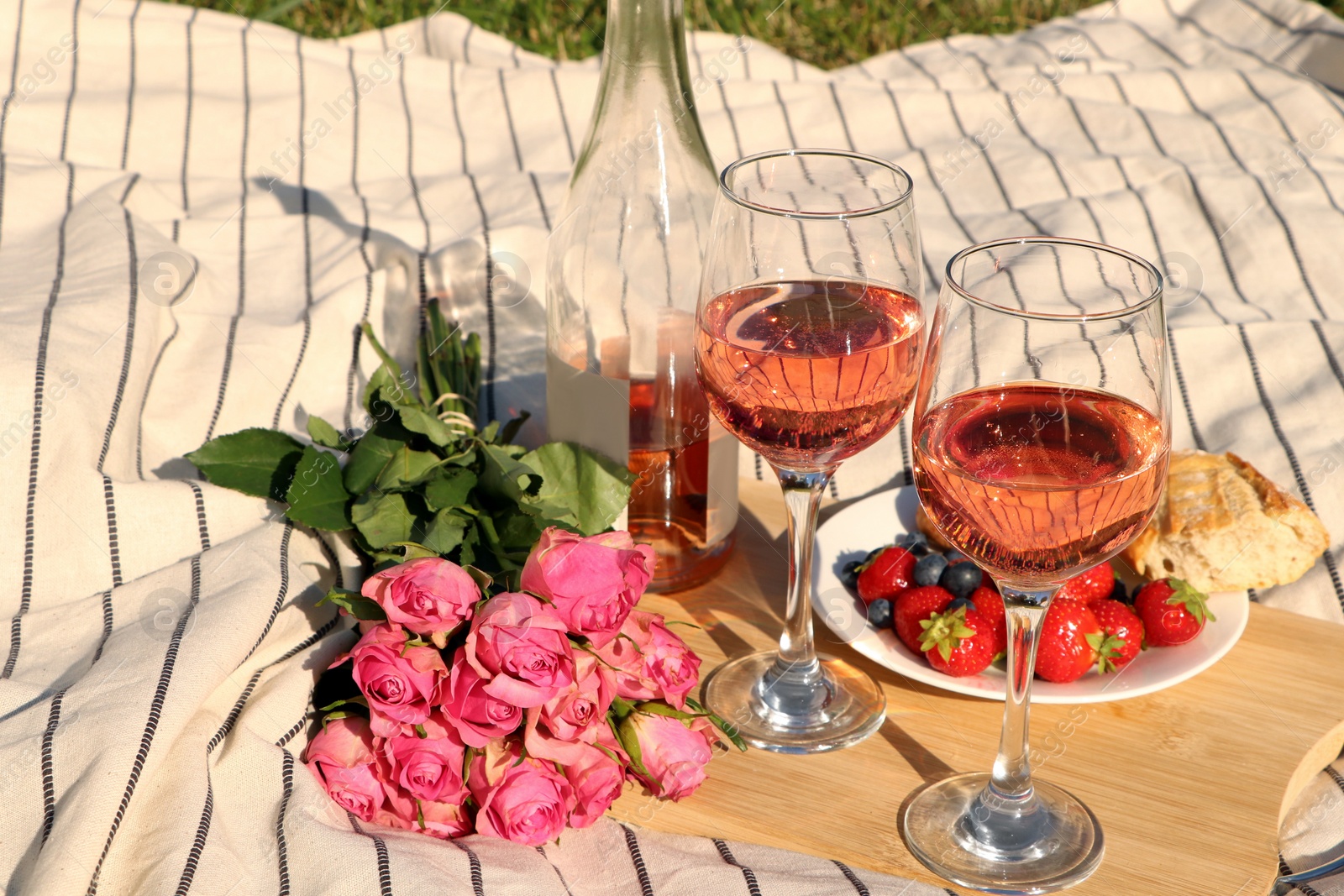 Photo of Glasses of delicious rose wine, flowers and food on picnic blanket outdoors