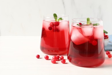 Tasty cranberry juice with ice cubes in glasses and fresh berries on white wooden table, closeup. Space for text