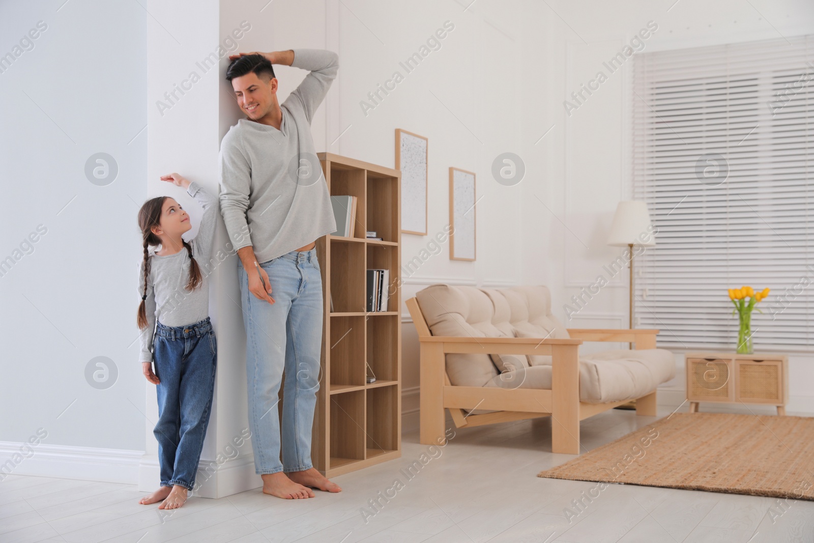 Photo of Little girl and father measuring their height near wall at home