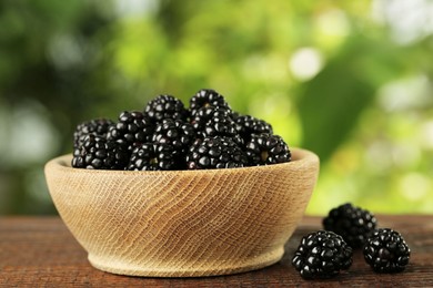 Photo of Bowl of fresh ripe blackberries on wooden table outdoors, closeup