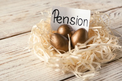 Golden eggs and card with word PENSION in nest on wooden background