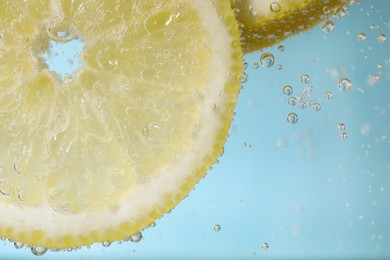 Juicy lemon slices in soda water against light blue background, closeup