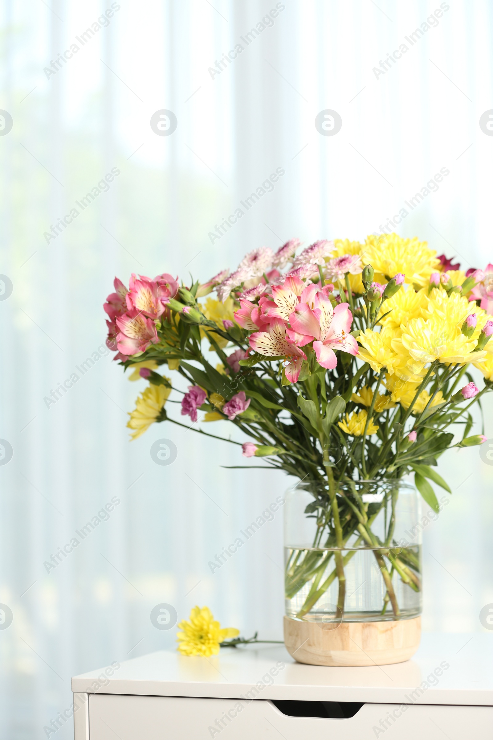 Photo of Vase with beautiful flowers on table near window indoors. Stylish element of interior design