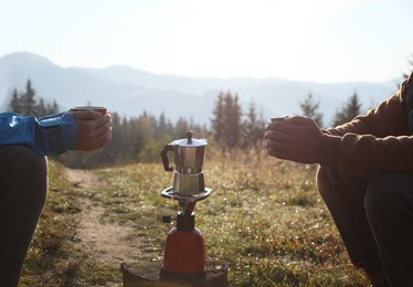 Photo of Young couple drinking coffee near camping tents in mountains, closeup