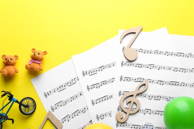 Photo of Baby songs. Music sheets, wooden notes and different toys on yellow background, flat lay
