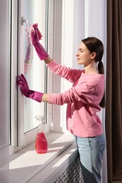 Photo of Young woman cleaning window glass with rag at home