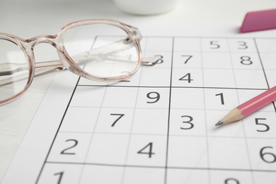 Photo of Sudoku, pencil and eyeglasses on white table, closeup