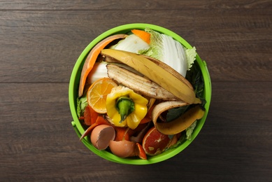 Photo of Trash bin with organic waste for composting on wooden background, top view
