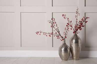 Photo of Hawthorn branches with red berries in vases near light wall indoors, space for text