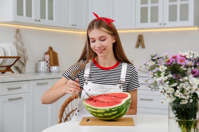 Photo of Beautiful teenage girl eating half of watermelon with spoon in kitchen