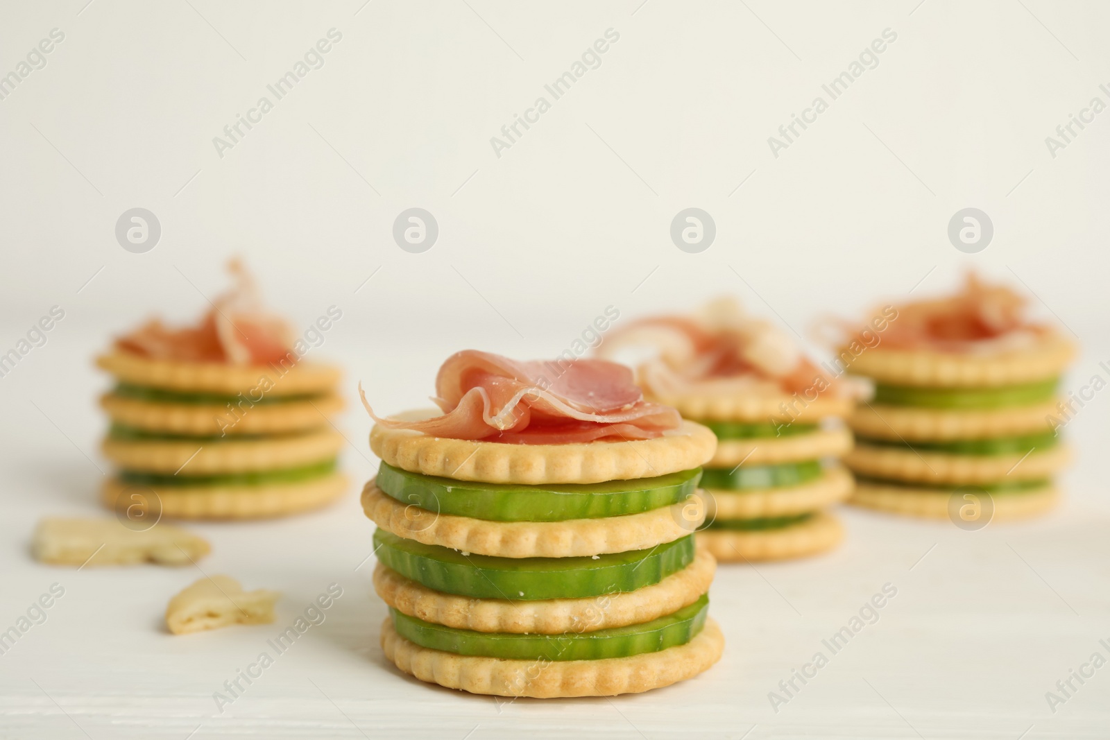 Photo of Delicious crackers with cucumber and prosciutto on white wooden table