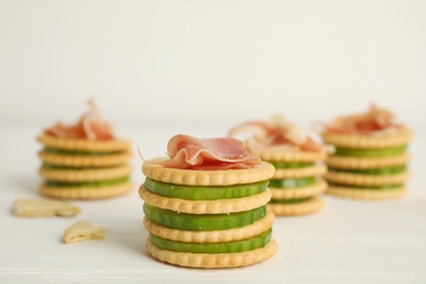 Delicious crackers with cucumber and prosciutto on white wooden table