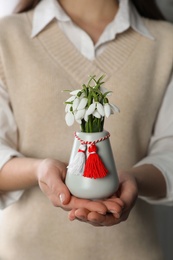 Photo of Woman holding vase with beautiful snowdrops and traditional martisor, closeup. Symbol of first spring day