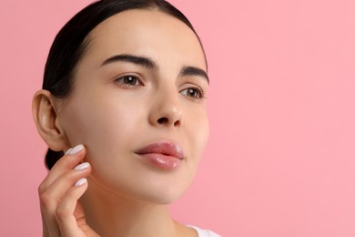 Woman with dry skin checking her face on pink background, space for text