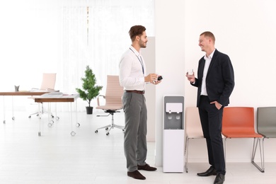 Men having break near water cooler at workplace. Space for text
