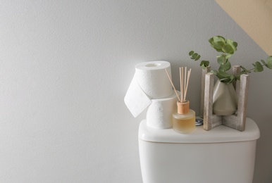 Decor elements and paper rolls on toilet tank near color wall, space for text. Bathroom interior