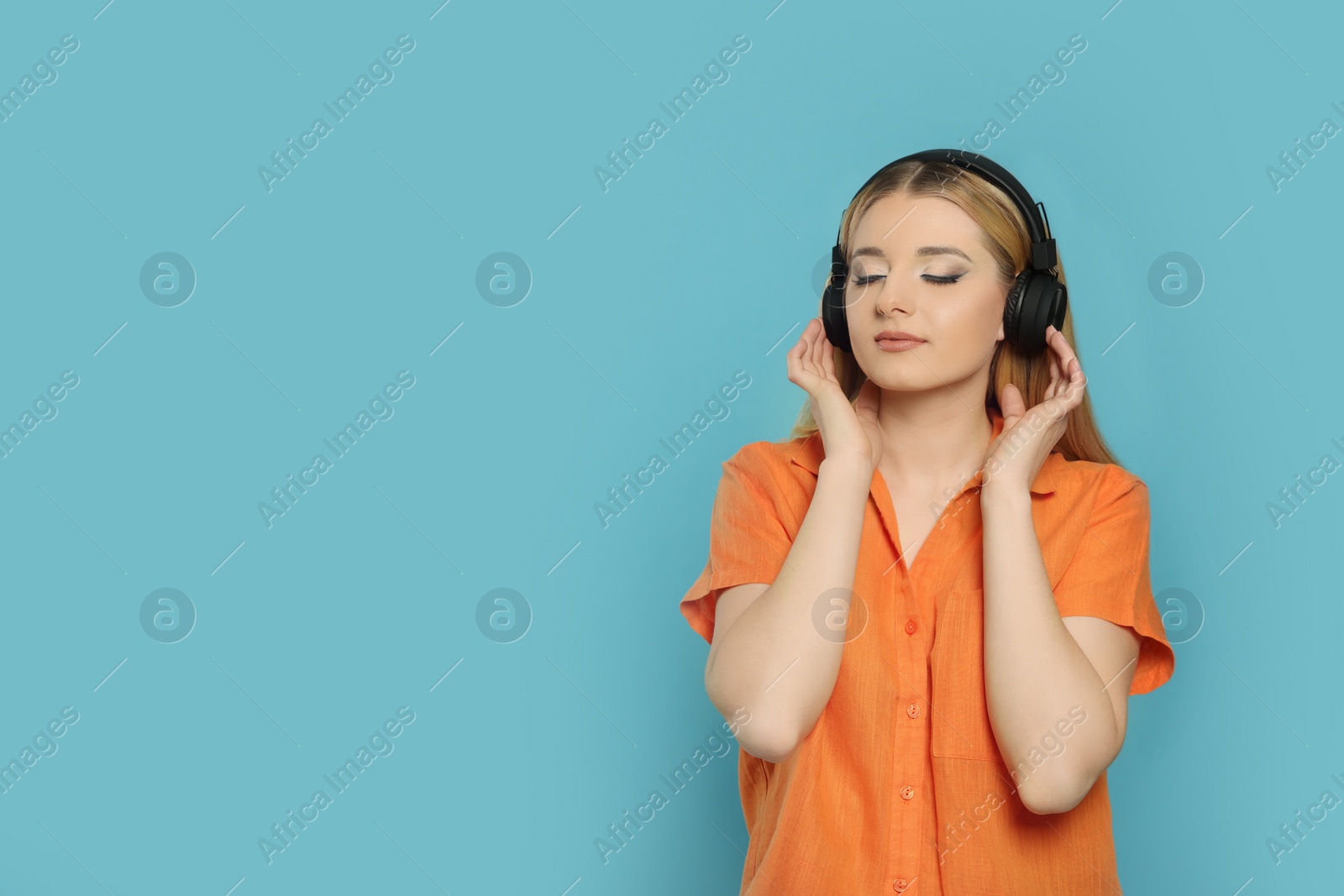 Photo of Beautiful woman in headphones enjoying music on light blue background. Space for text