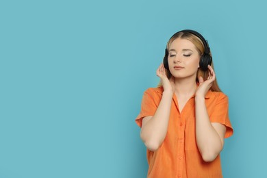 Beautiful woman in headphones enjoying music on light blue background. Space for text