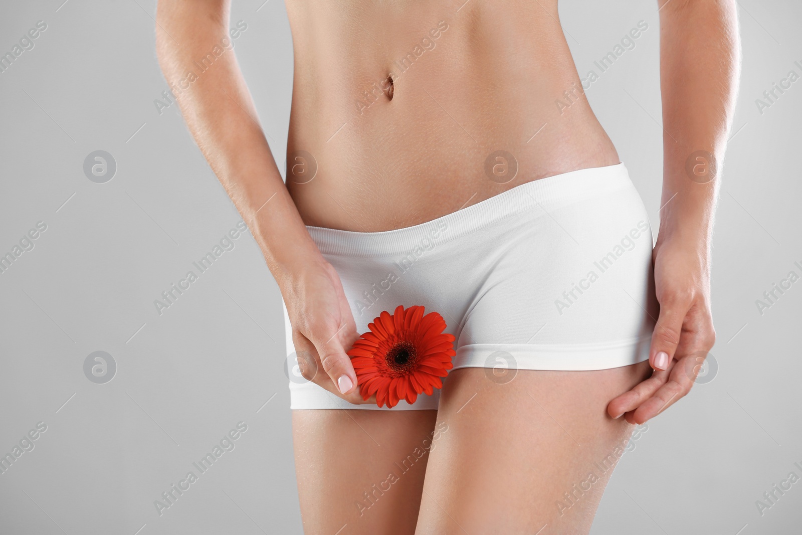 Photo of Young woman with gerbera flower on grey background. Gynecology concept
