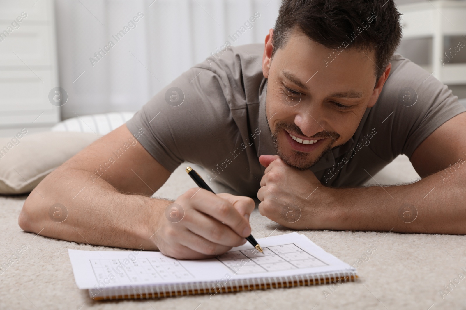 Photo of Man solving sudoku puzzle on floor at home