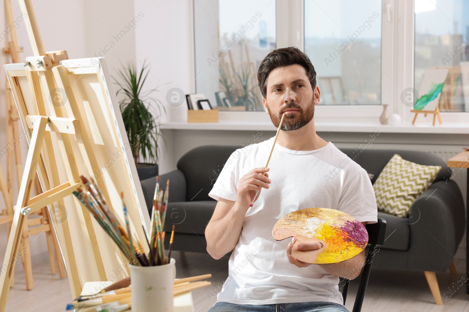 Photo of Man painting in studio. Using easel to hold canvas