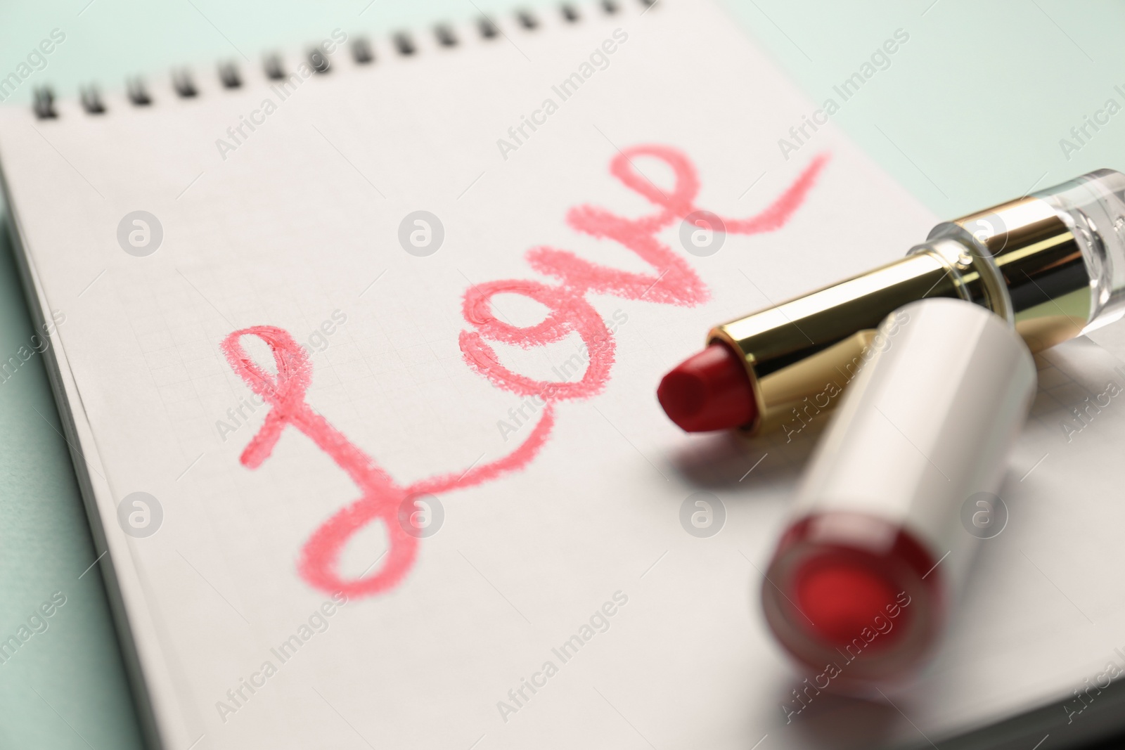 Photo of Notebook with word Love and red lipstick on turquoise background, closeup