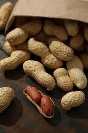 Photo of Paper bag with fresh unpeeled peanuts on wooden table, closeup