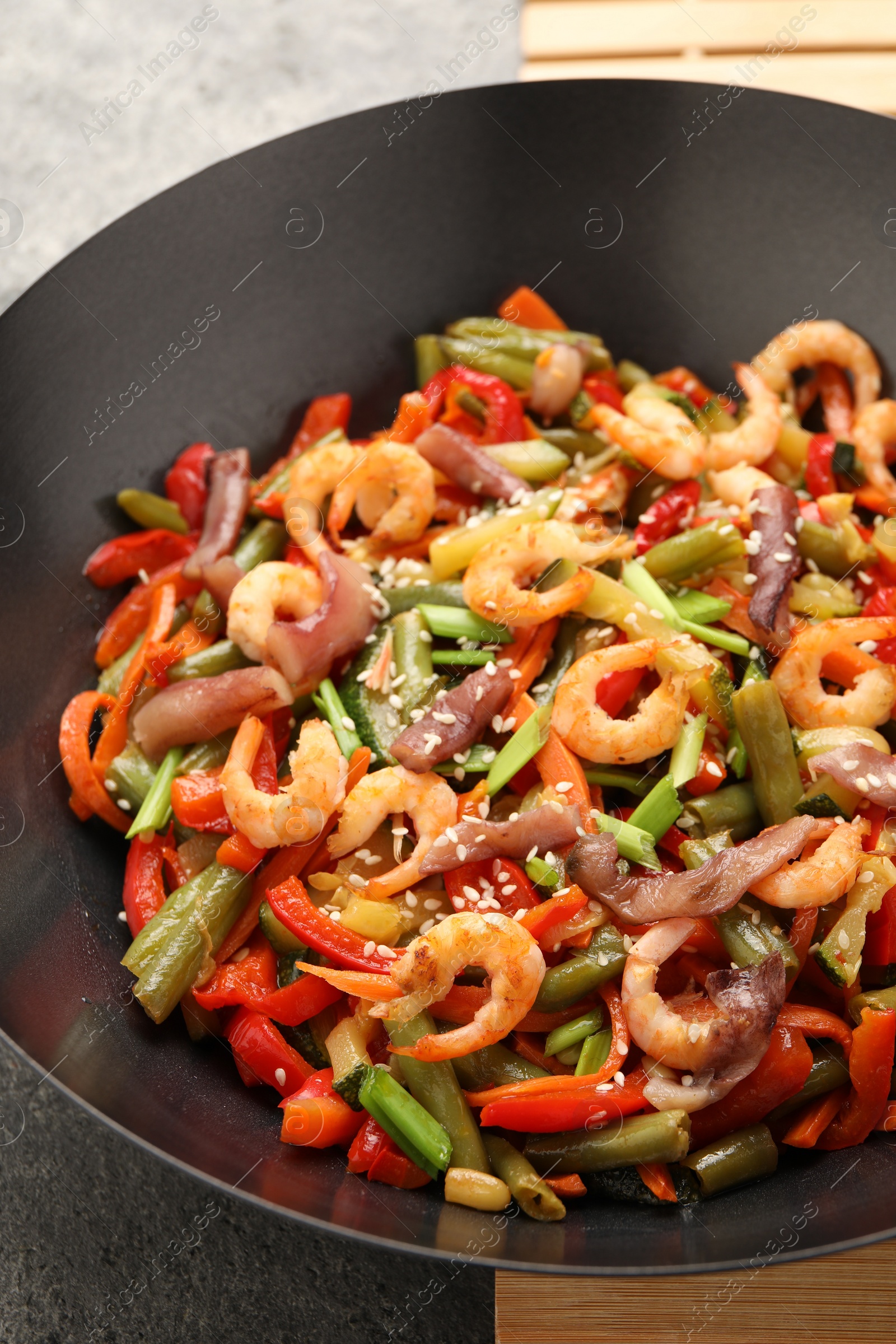 Photo of Shrimp stir fry with vegetables in wok on grey table, closeup