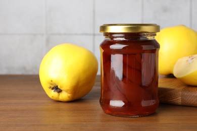 Photo of Tasty homemade quince jam in jar and fruits on wooden table, closeup. Space for text