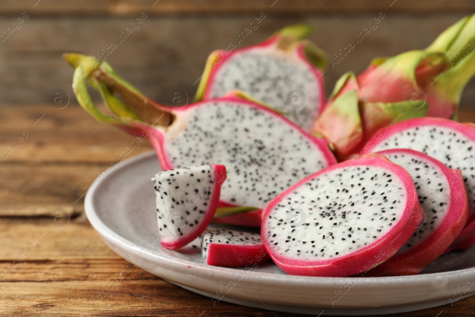 Photo of Delicious cut and whole dragon fruits (pitahaya) on wooden table, closeup