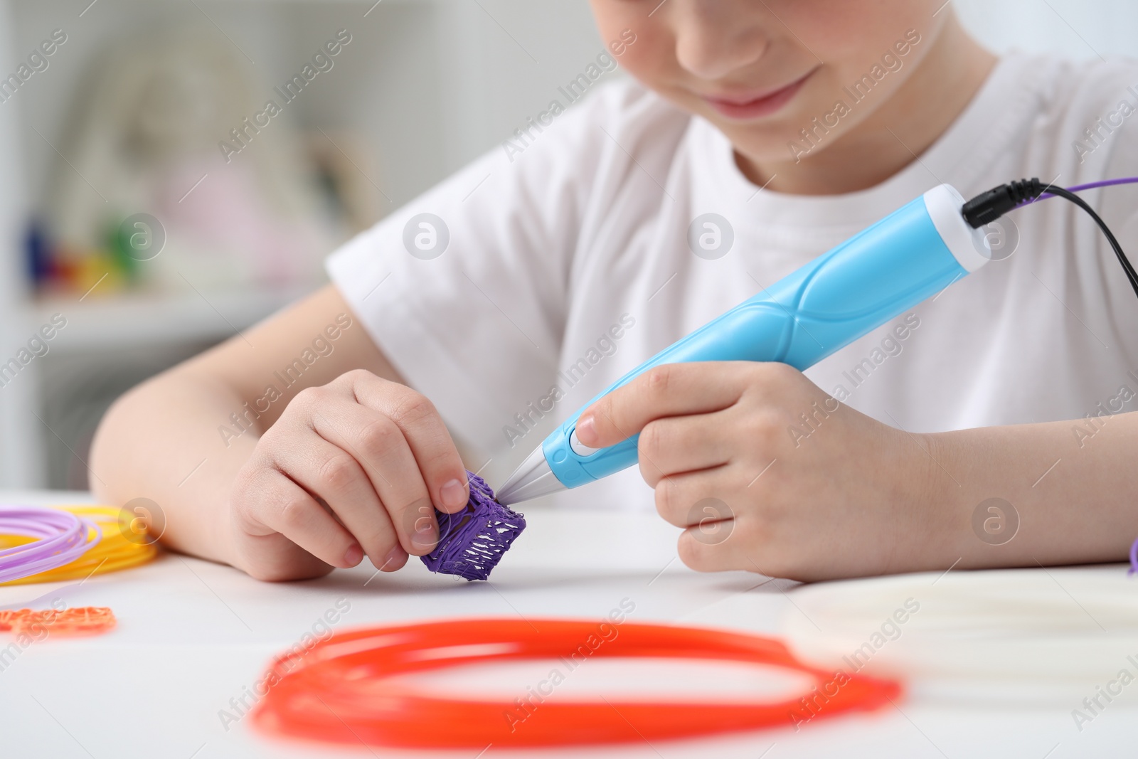 Photo of Girl drawing with stylish 3D pen at white table indoors, closeup